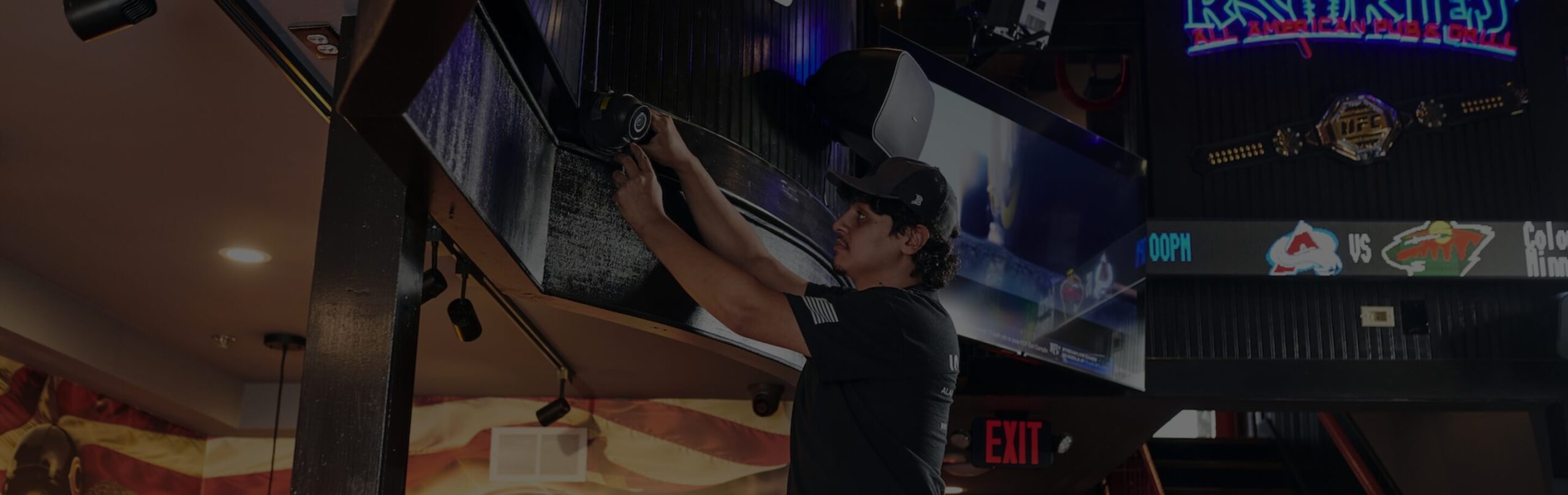 Technician on a ladder installing a security camera on a ceiling beam in a restaurant and bar